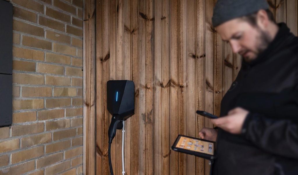Techniker konfiguriert eine schwarze Easee-Ladestation an einer Holzwand